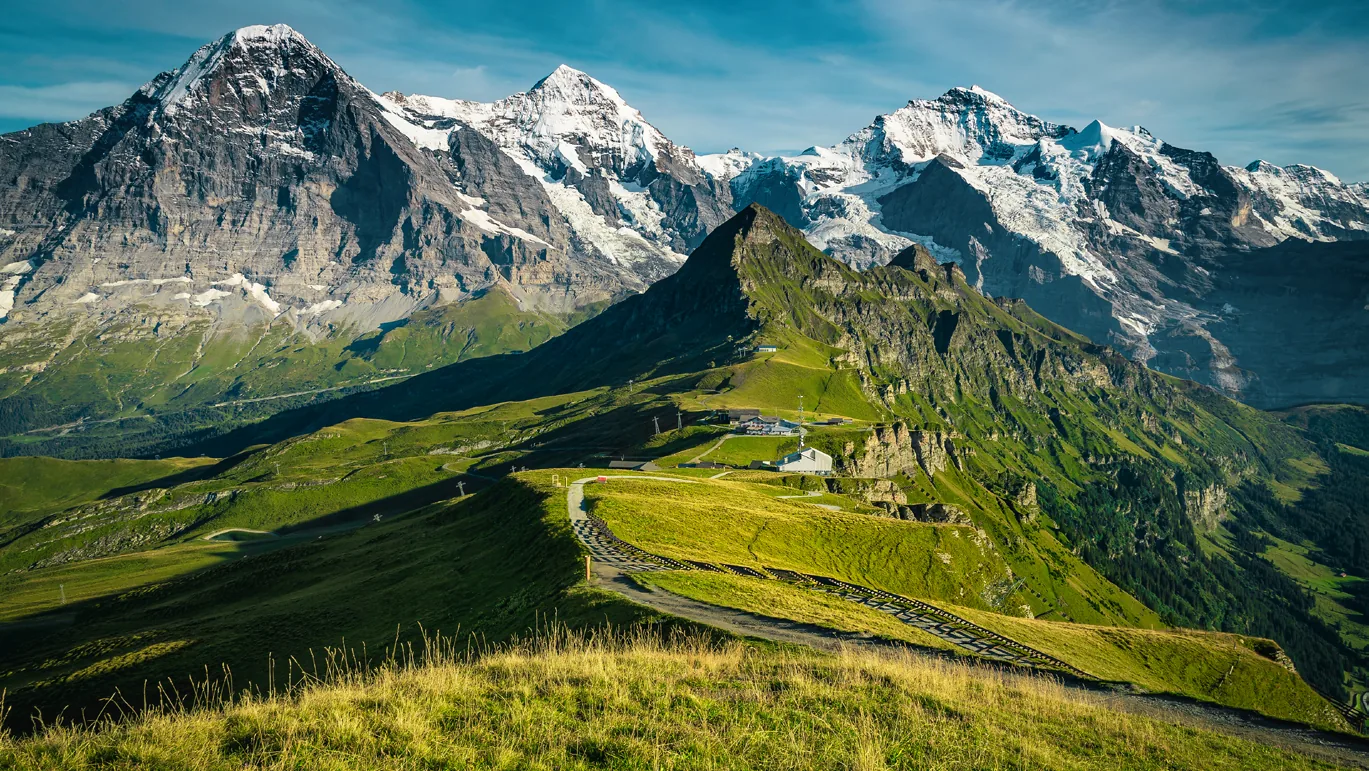 Green alpine pastures below snow-capped mountains